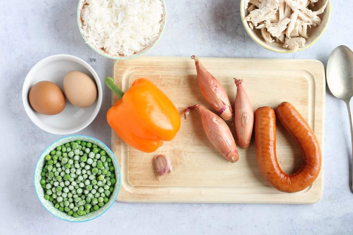 Ingredients for recipe including shallots, garlic, pepper, eggs, cooked rice, frozen peas and cooked chicken.