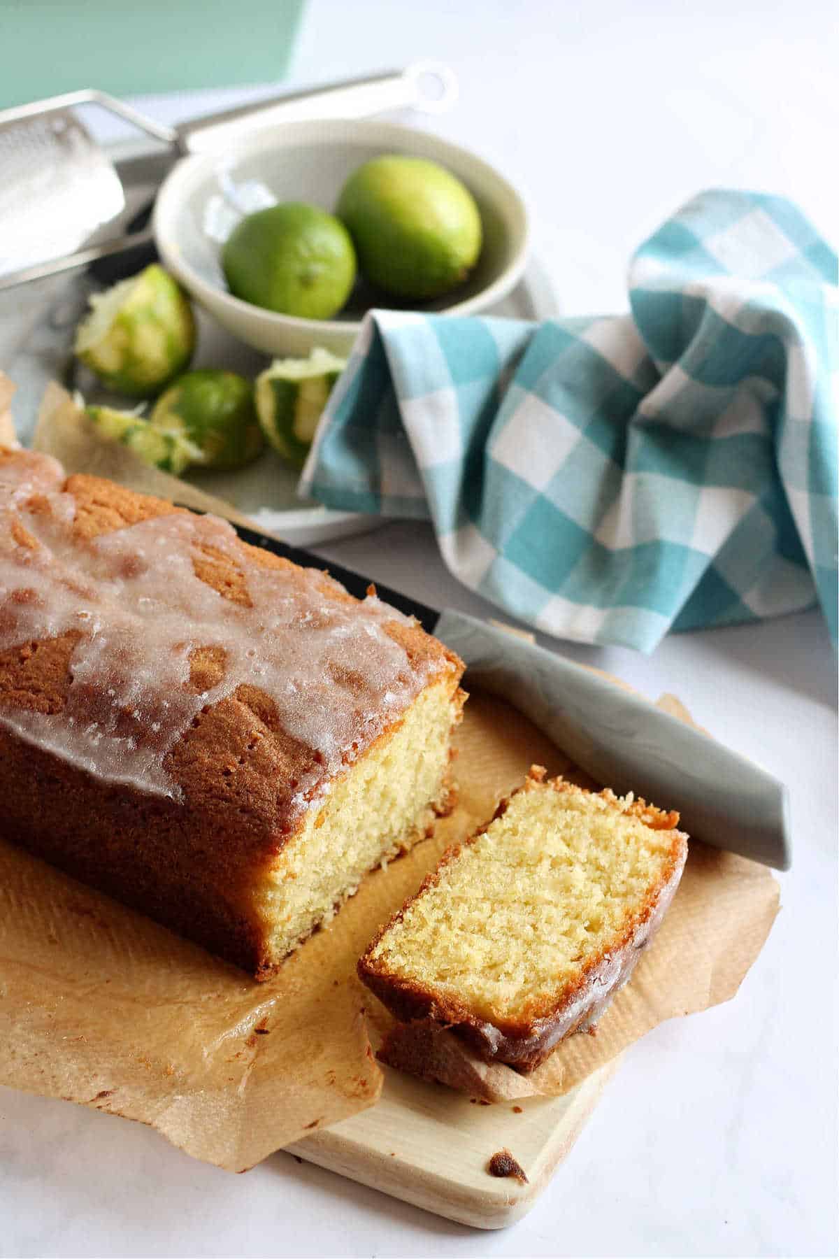 A slice of lime and coconut loaf cake cut off the end of the cake, with limes in the background