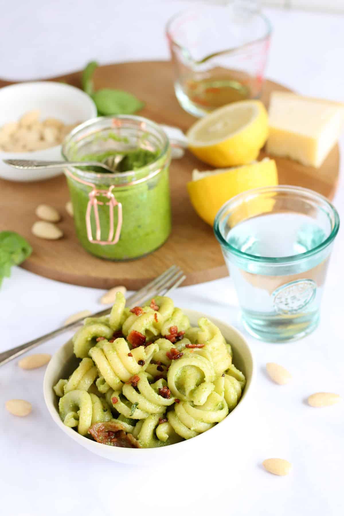 A bowl of pasta with ingredients for a homemade basil sauce in the background.