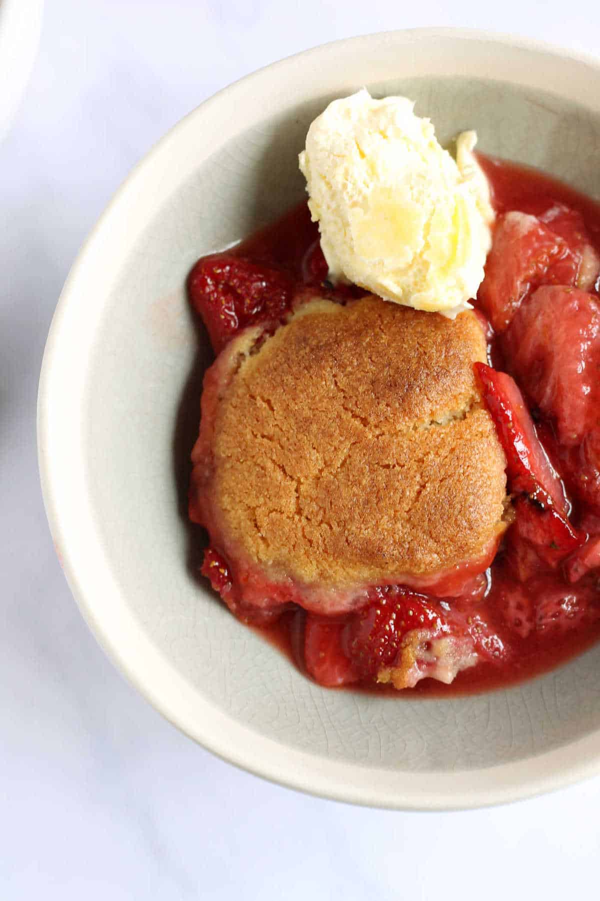 An overhead shot of a bowl of strawberry cobbler with clotted cream