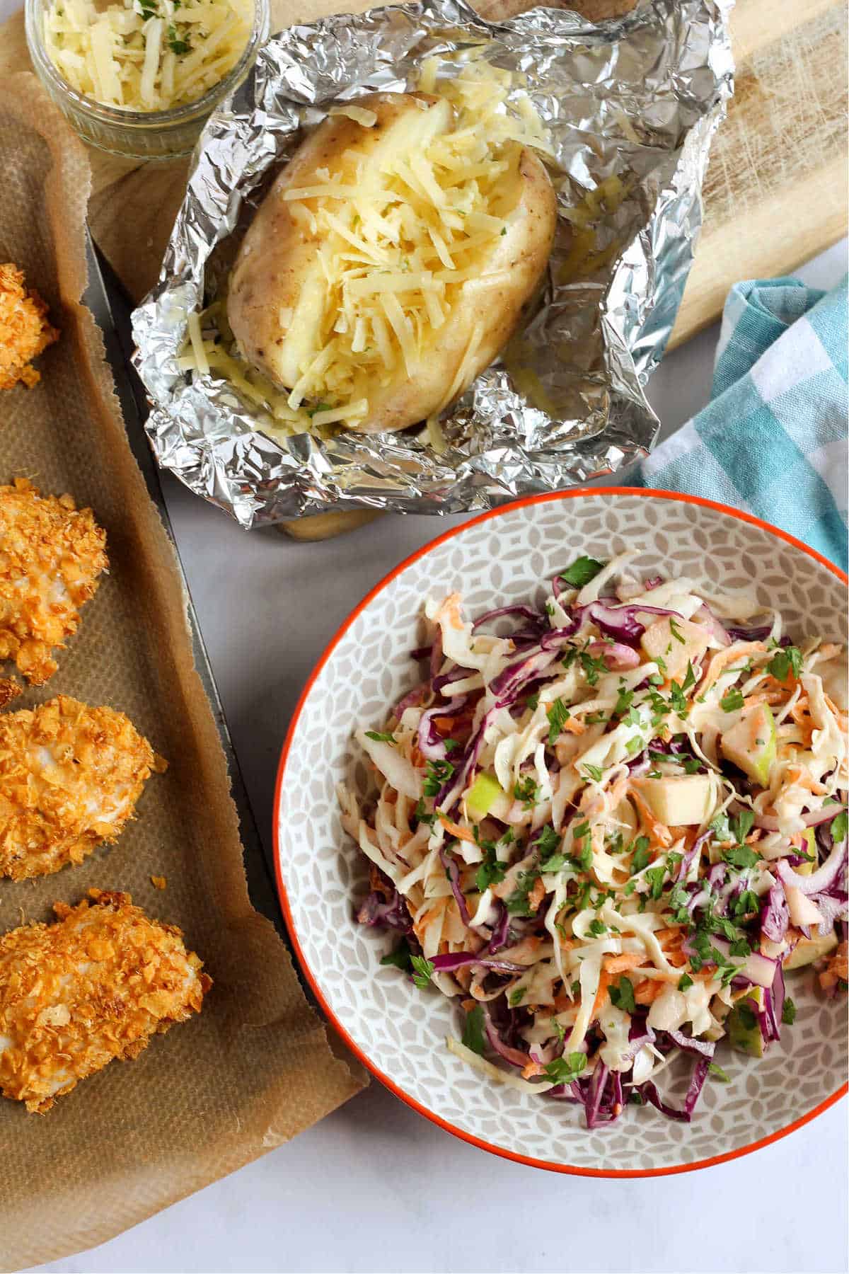 Apple coleslaw in a bowl with a baked potato and cornflake chicken nuggets