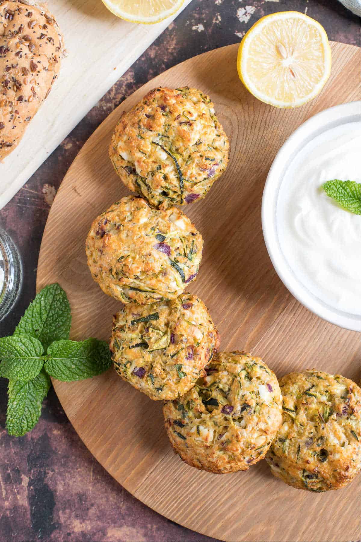 Overhead shot of courgette and feta burgers on a serving board with a minty yogurt dip and bread.