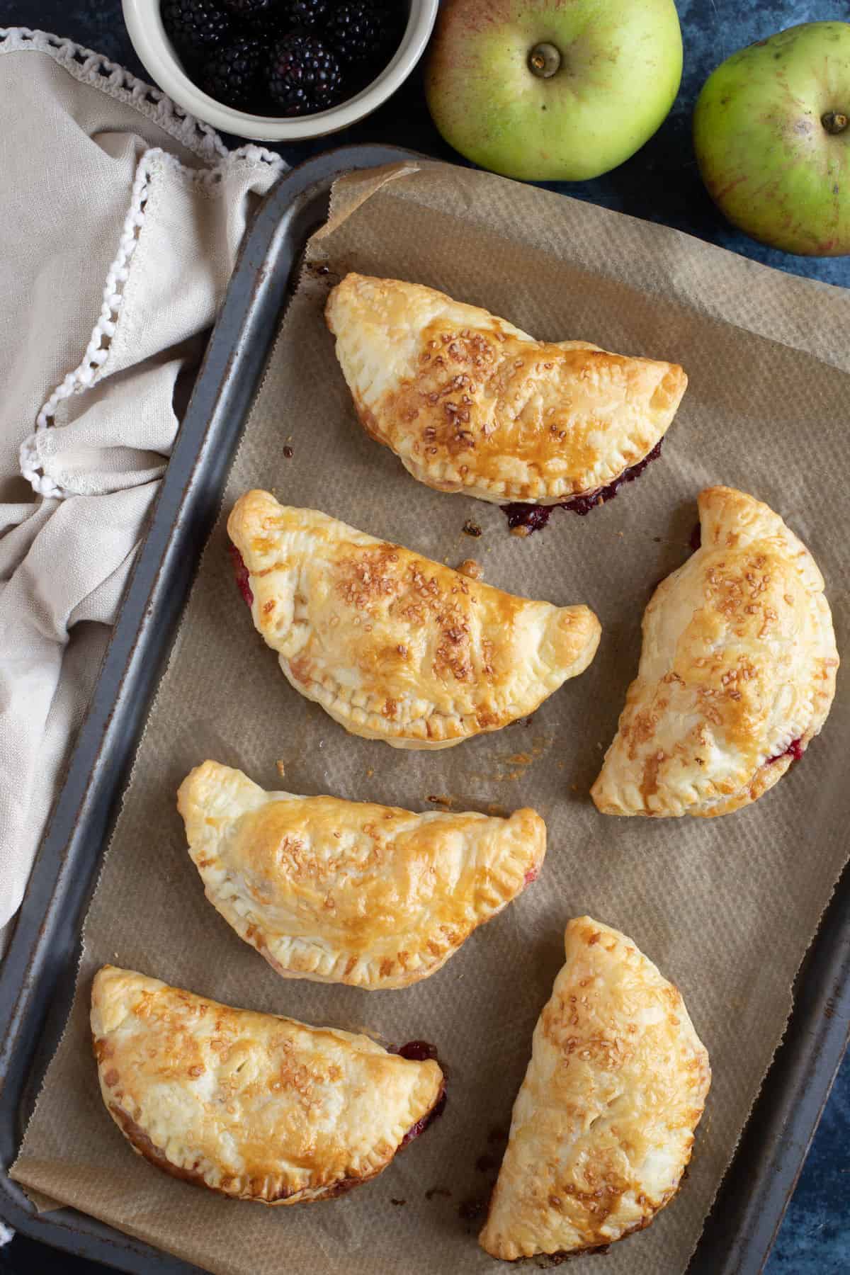 Overhead shot of apple and blackberry turnovers on a baking tray.