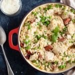 Chicken and chorizo risotto in a red pan with grated Parmesan.