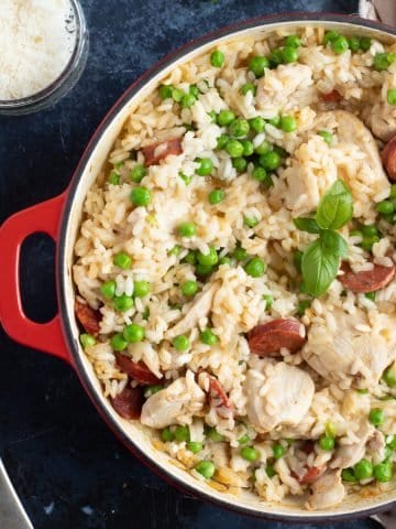 Chicken and chorizo risotto in a red pan with grated Parmesan.
