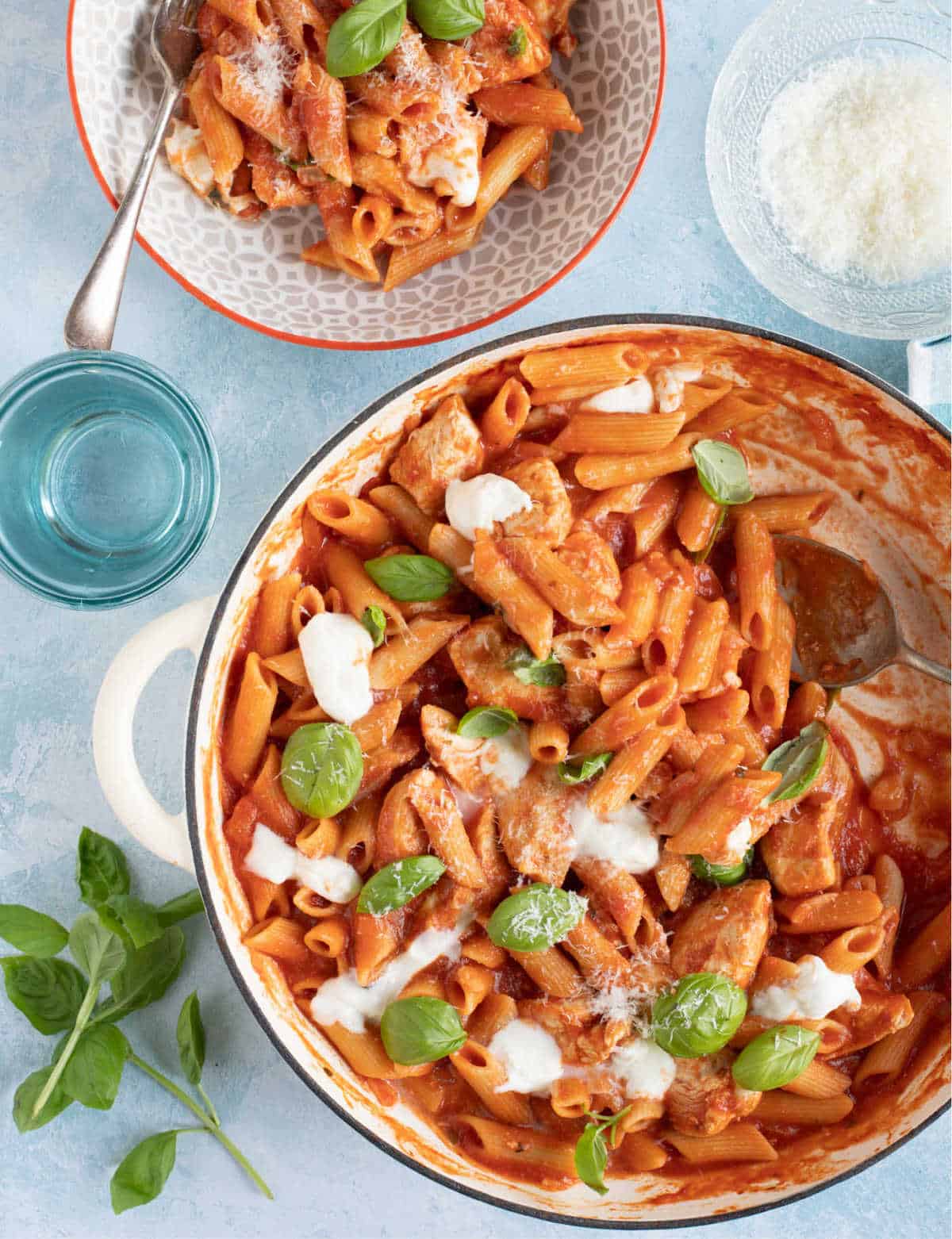 Overhead shot of chicken penne arrabbiata  with basil leaves and mozzarella.