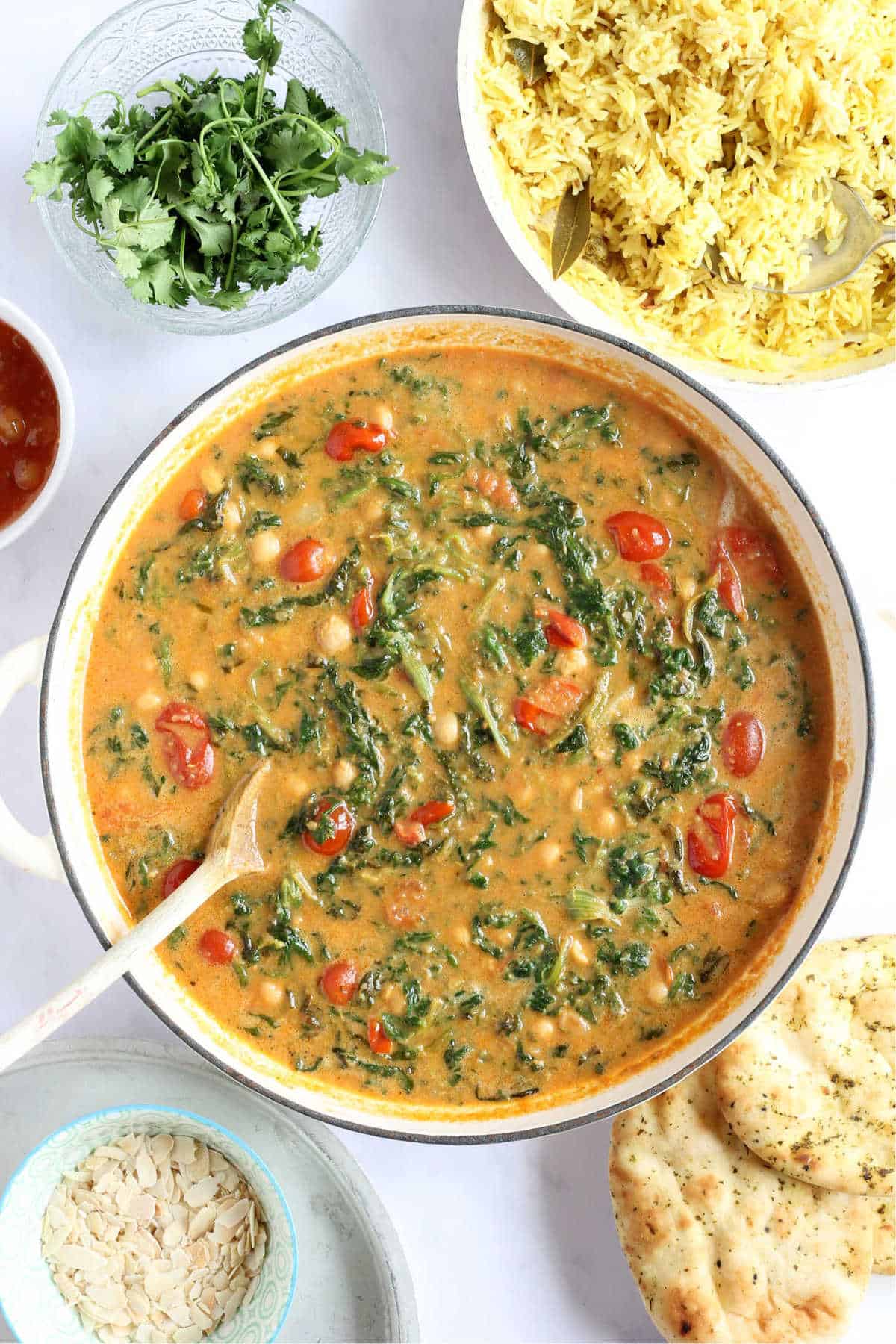 A pan of chickpea and spinach curry with naan breads and pilau rice.