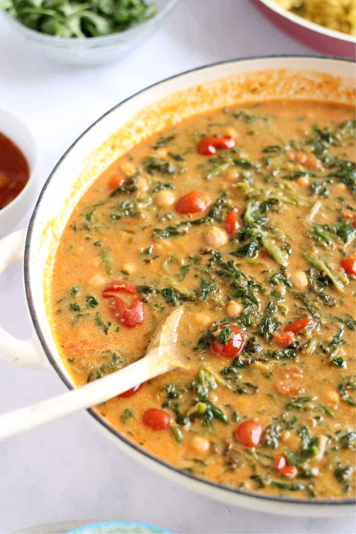 Creamy vegan chickpea and spinach curry being stirred with a wooden spoon.