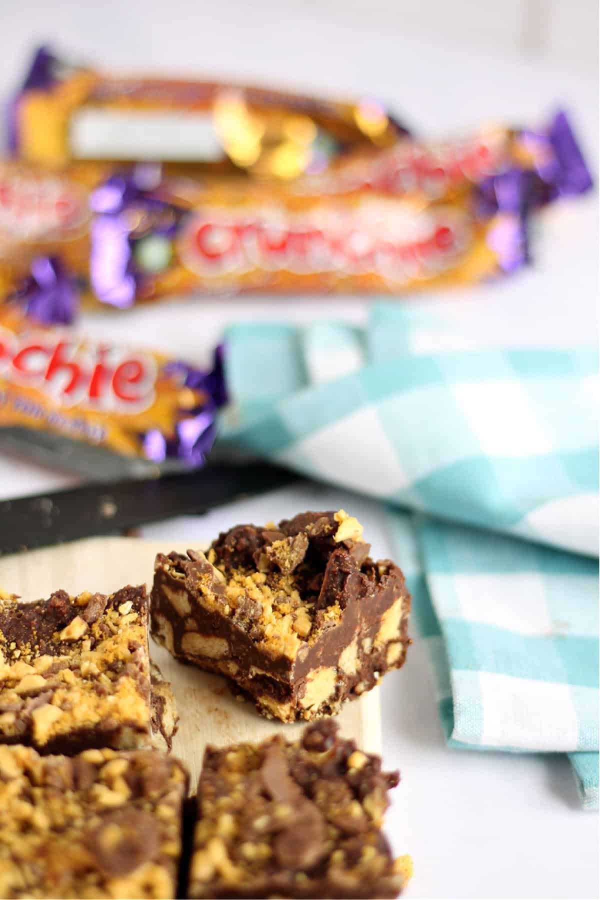 A slice of crunchie tiffin in focus, with crunchie wrappers in background.