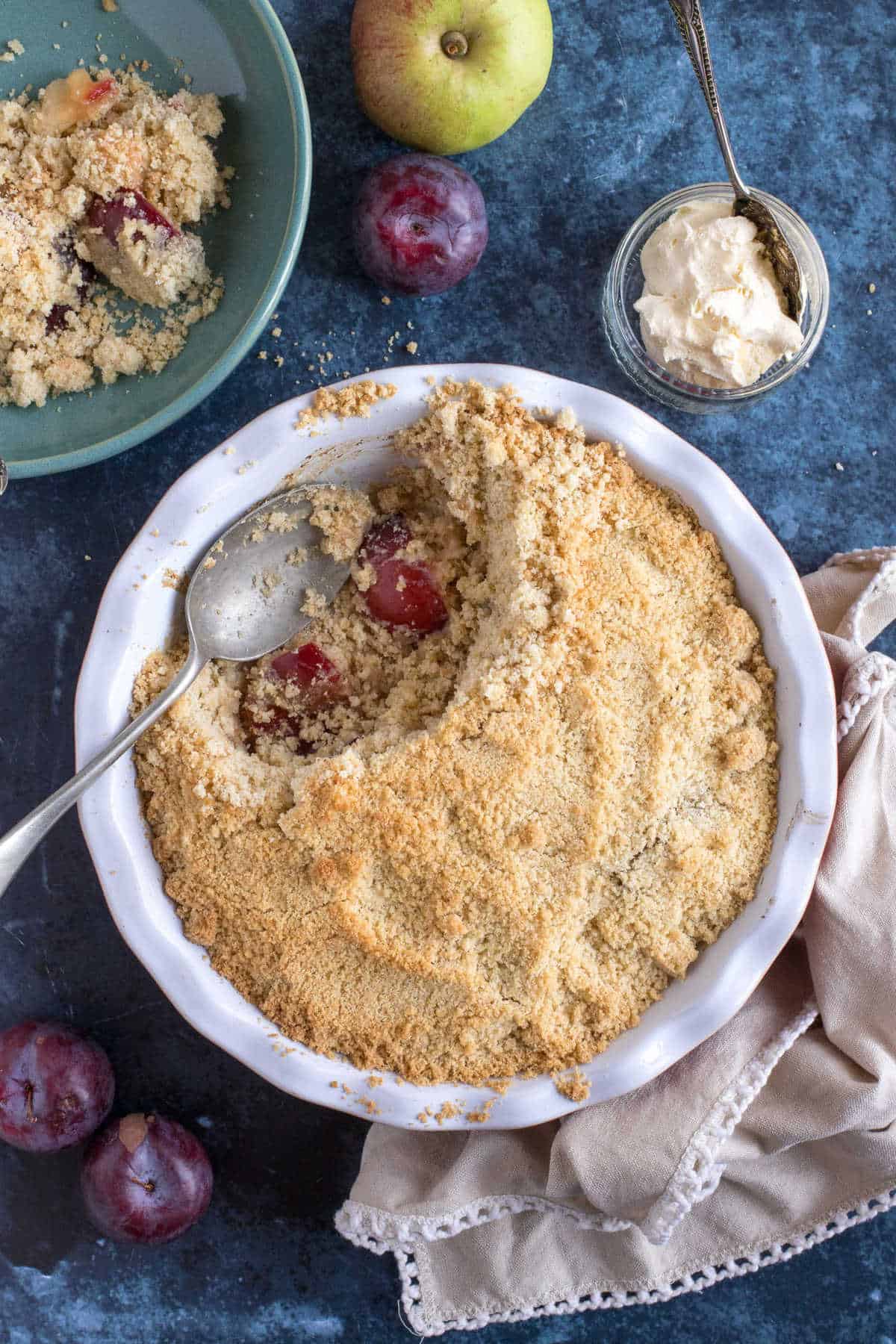 Plum and apple crumble in a red pie dish.