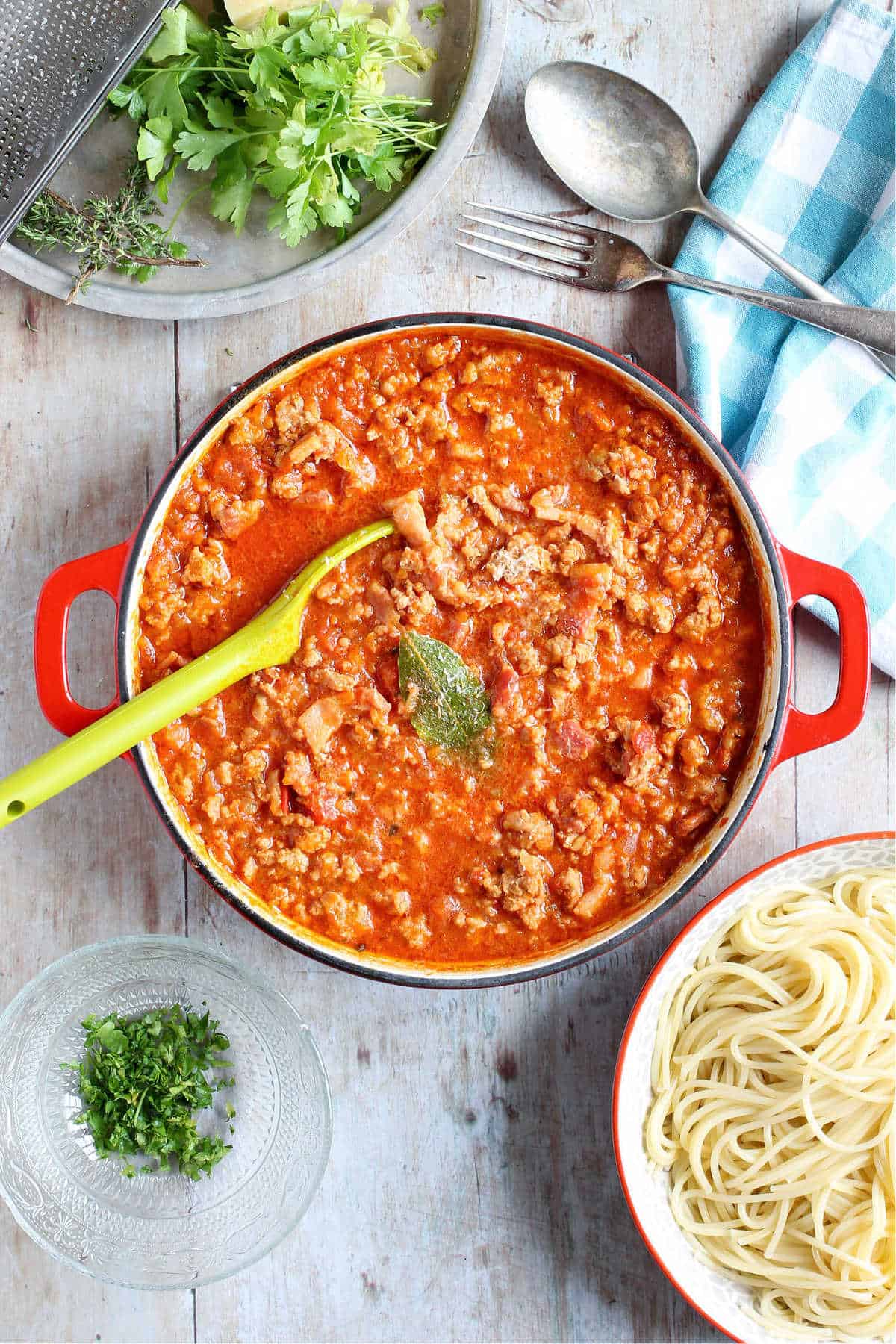 Overhead shot of a pan of pork bolognese with fresh herbs and spaghetti.