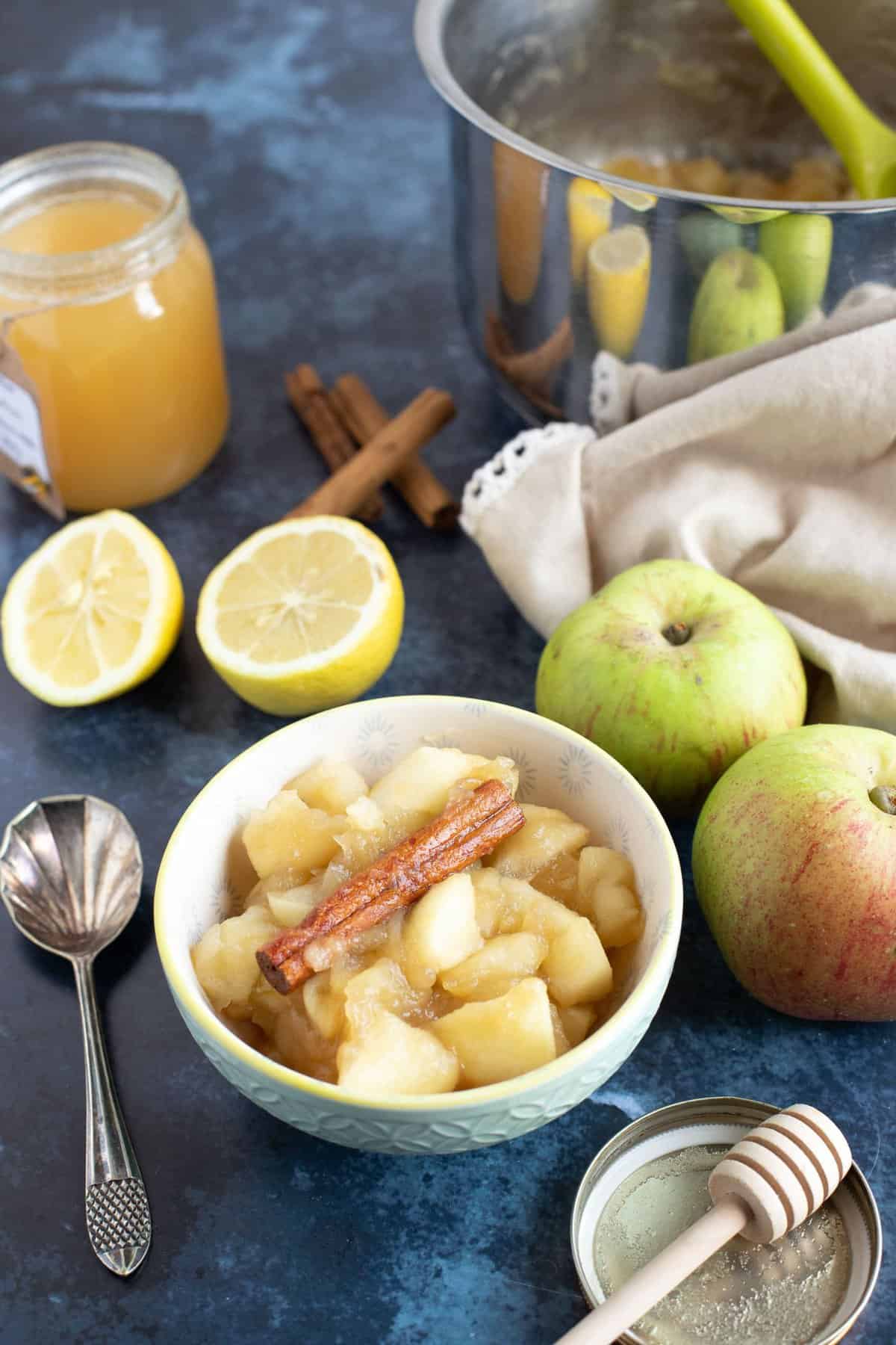 Stewed apples in a bowl with a pan of stewed apples behind.