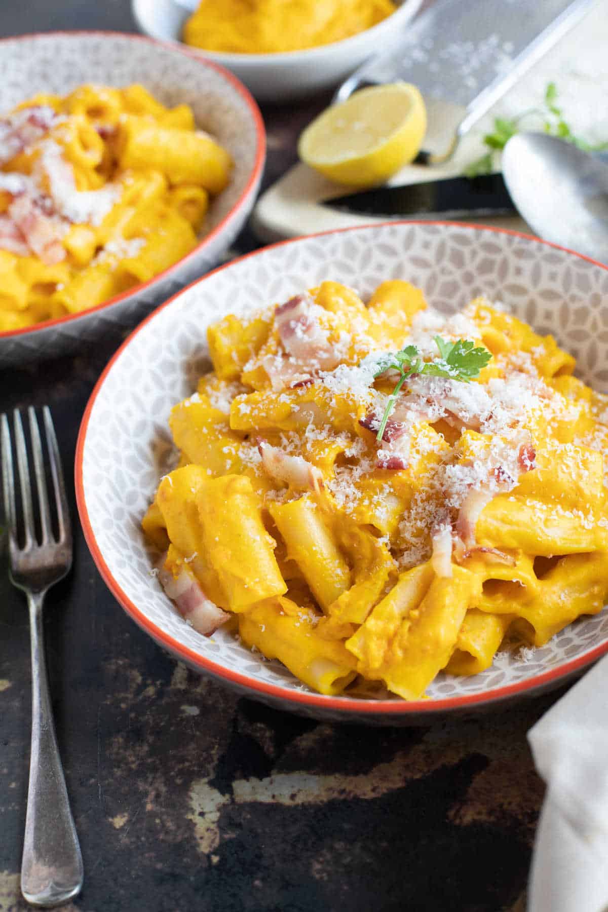 Pumpkin and bacon pasta in serving bowls sprinkled with Parmesan.