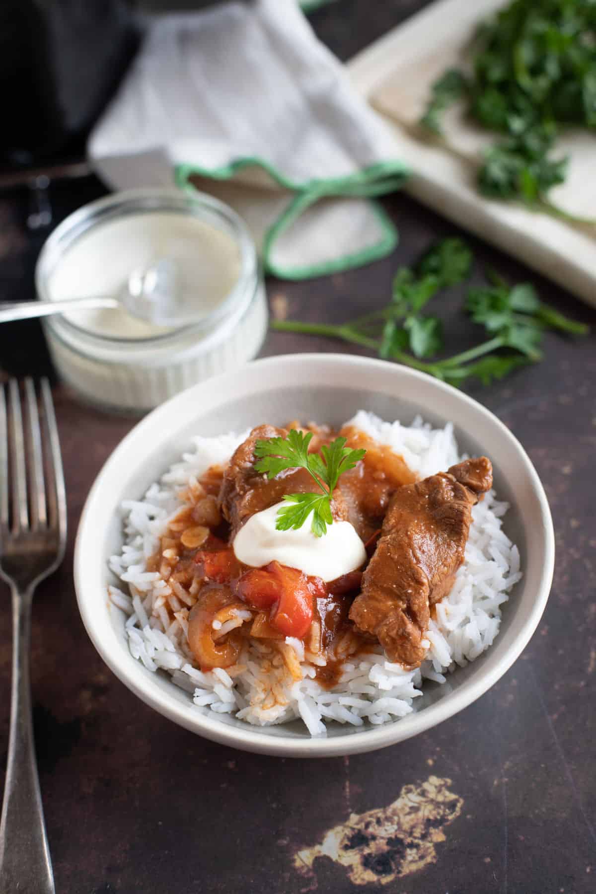 Slow cooker beef goulash served on a bed of rice with soured cream and parsley.