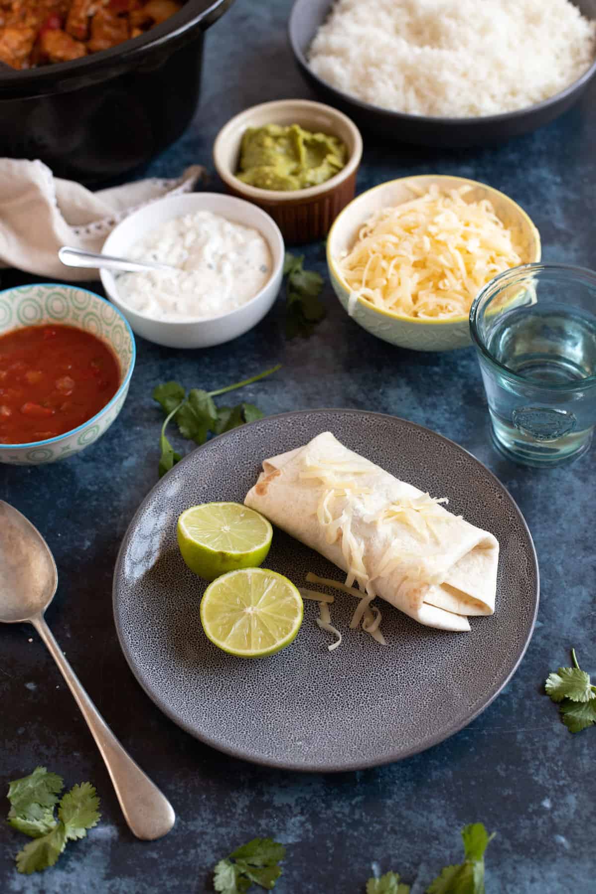 A fajita wrap on a plate with grated cheddar, sour cream and salsa.