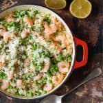 Prawn and pea risotto in a red pan with lemon wedges