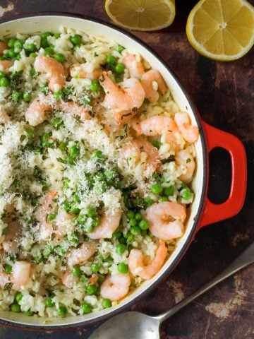 Prawn and pea risotto in a red pan with lemon wedges
