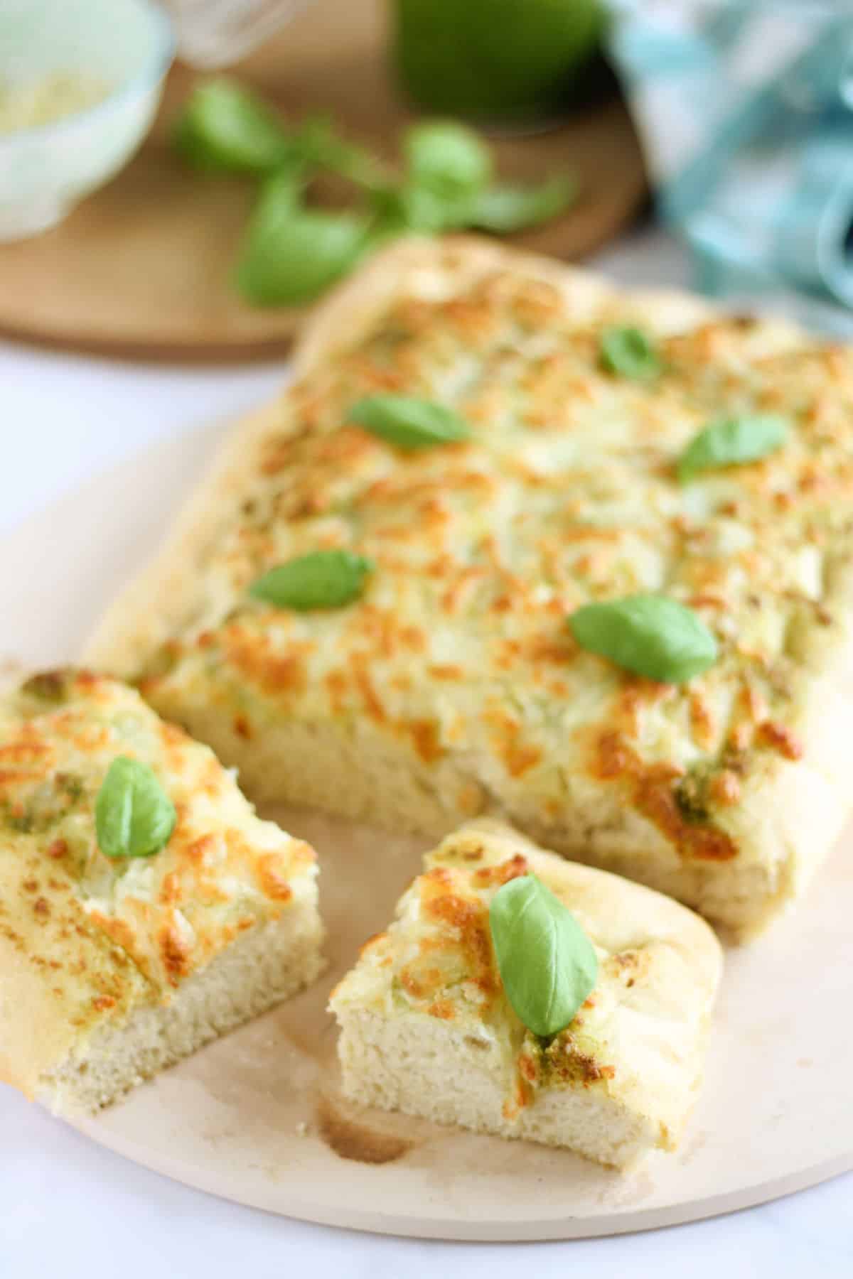 Slices of pesto focaccia scattered with fresh basil.