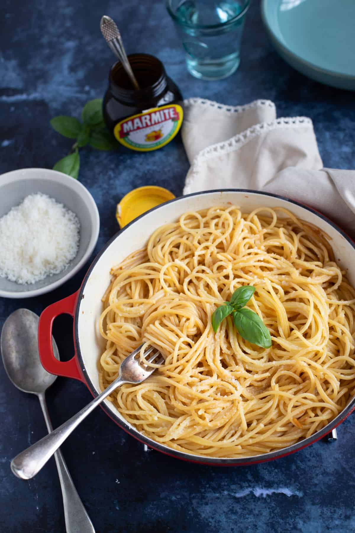 A pan of marmite spaghetti with a jar of marmite in the background.