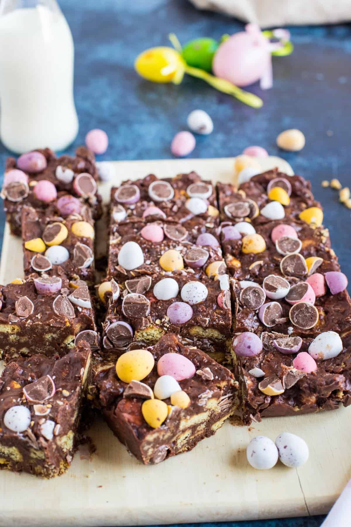 Slices of chocolate tiffin studded with mini eggs on a wooden board.