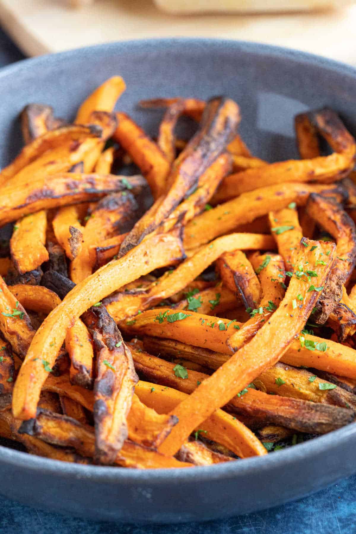 Sweet potato fries in a grey bowl served with chopped parsley.