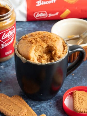 Biscoff mug cake in a large black mug sprinkled with lotus biscuit crumbs.