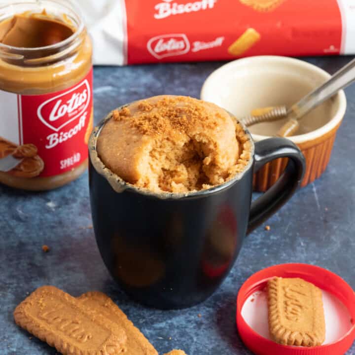 Biscoff mug cake in a large black mug sprinkled with lotus biscuit crumbs.