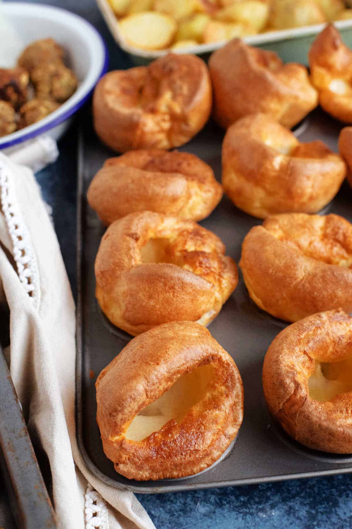 A tray of Yorkshire puddings with roast potatoes in the background.