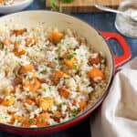 Butternut squash and bacon risotto in a red pan garnished with parsley.