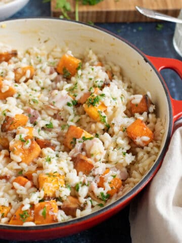 Butternut squash and bacon risotto in a red pan garnished with parsley.