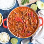 A pan of mild chilli with lime wedges, rice and tortilla chips.