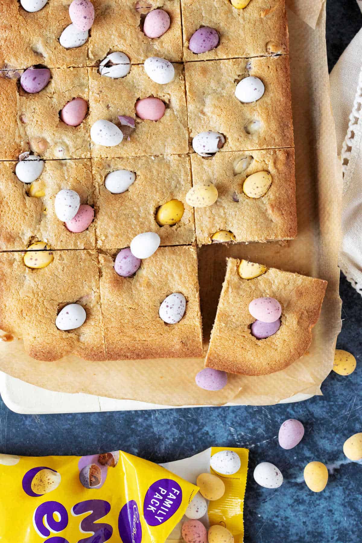 Chocolate mini egg cookie bars cut into squares on a wooden board.