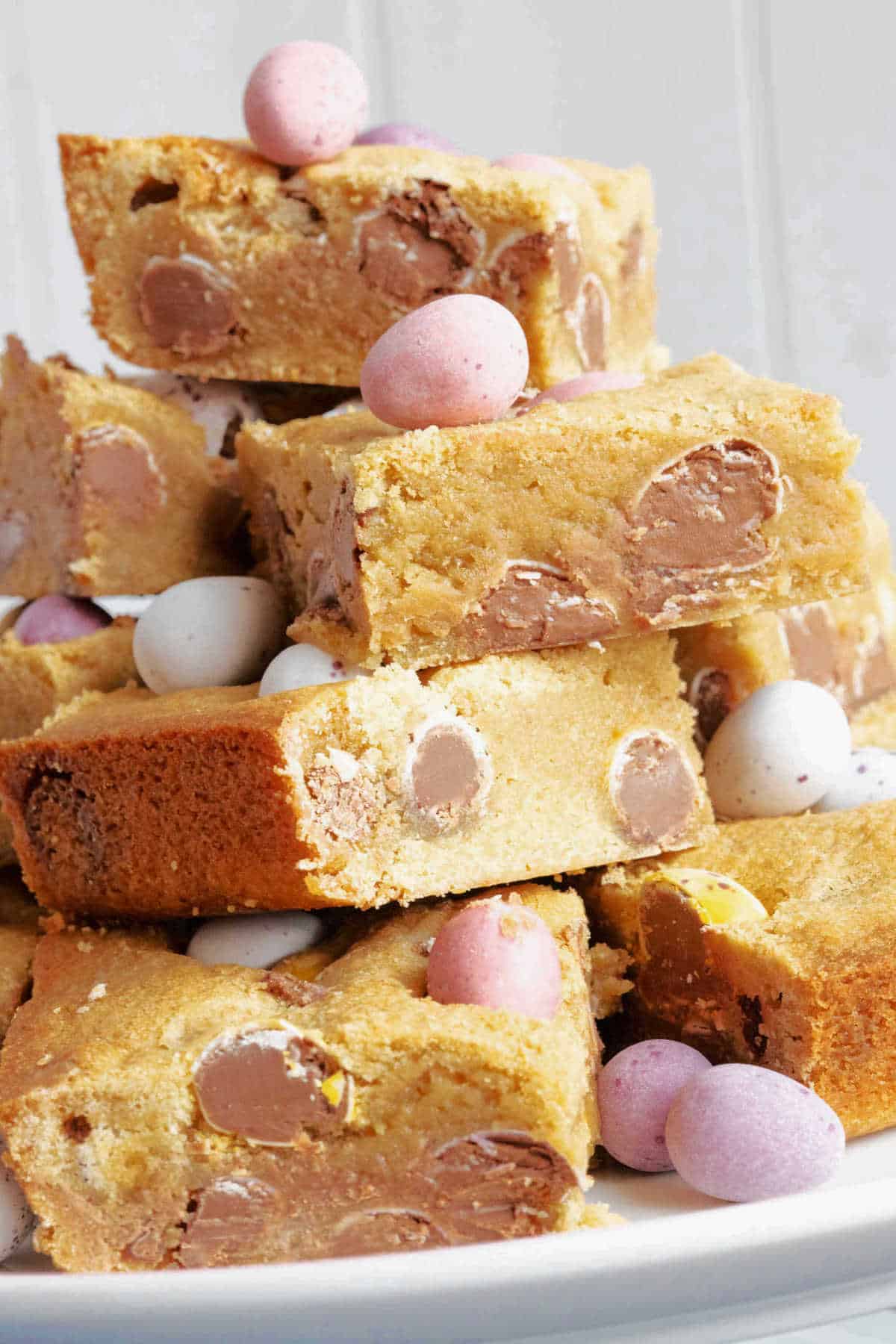 Mini egg cookie bars stacked on a cake stand with extra mini eggs for decoration.
