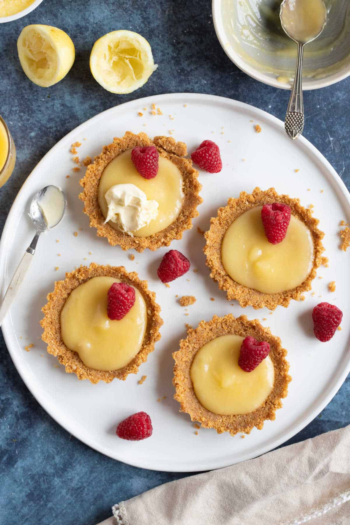 No bake lemon curd tartlets with a biscuit base on a white serving platter.