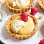 A lemon curd tartlet topped with raspberries and cream.