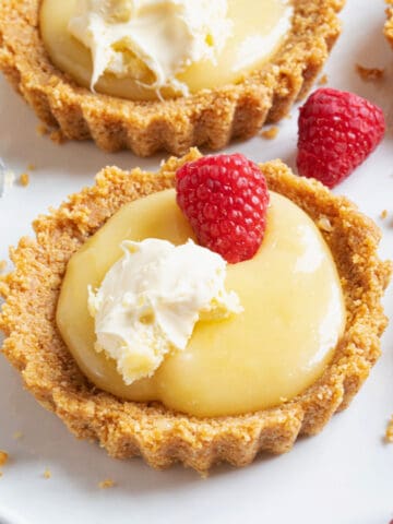 A lemon curd tartlet topped with raspberries and cream.