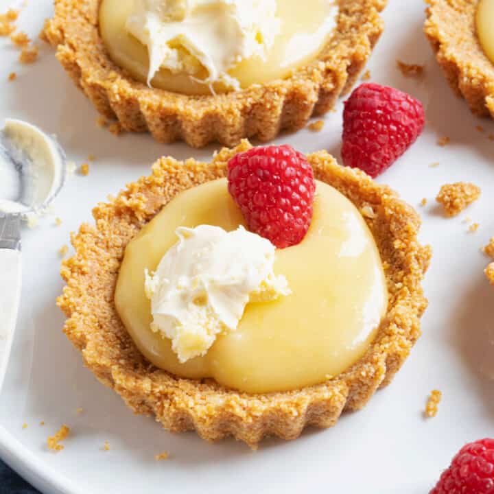 A lemon curd tartlet topped with raspberries and cream.