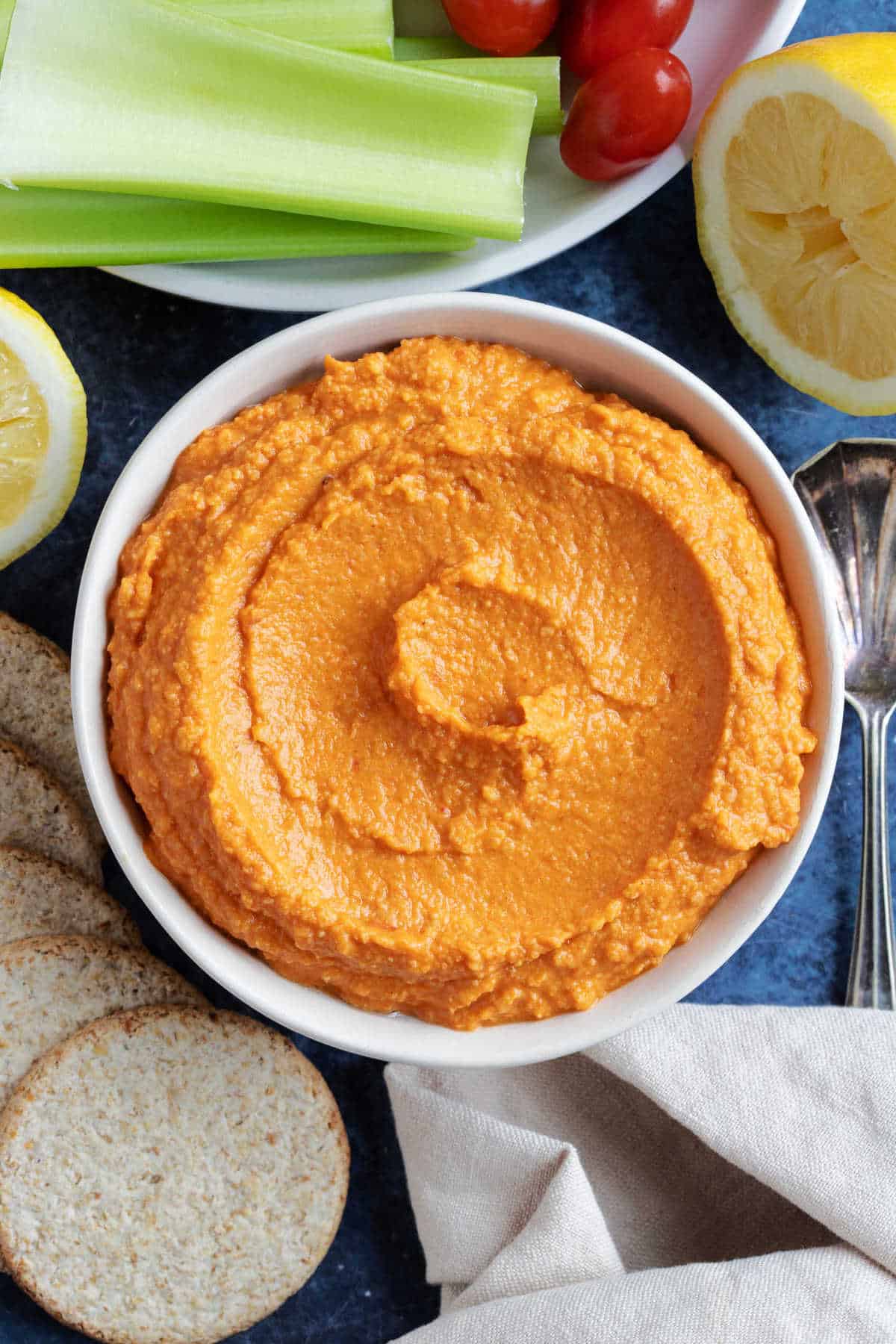 Roasted red pepper hummus in a serving dish with celery sticks.