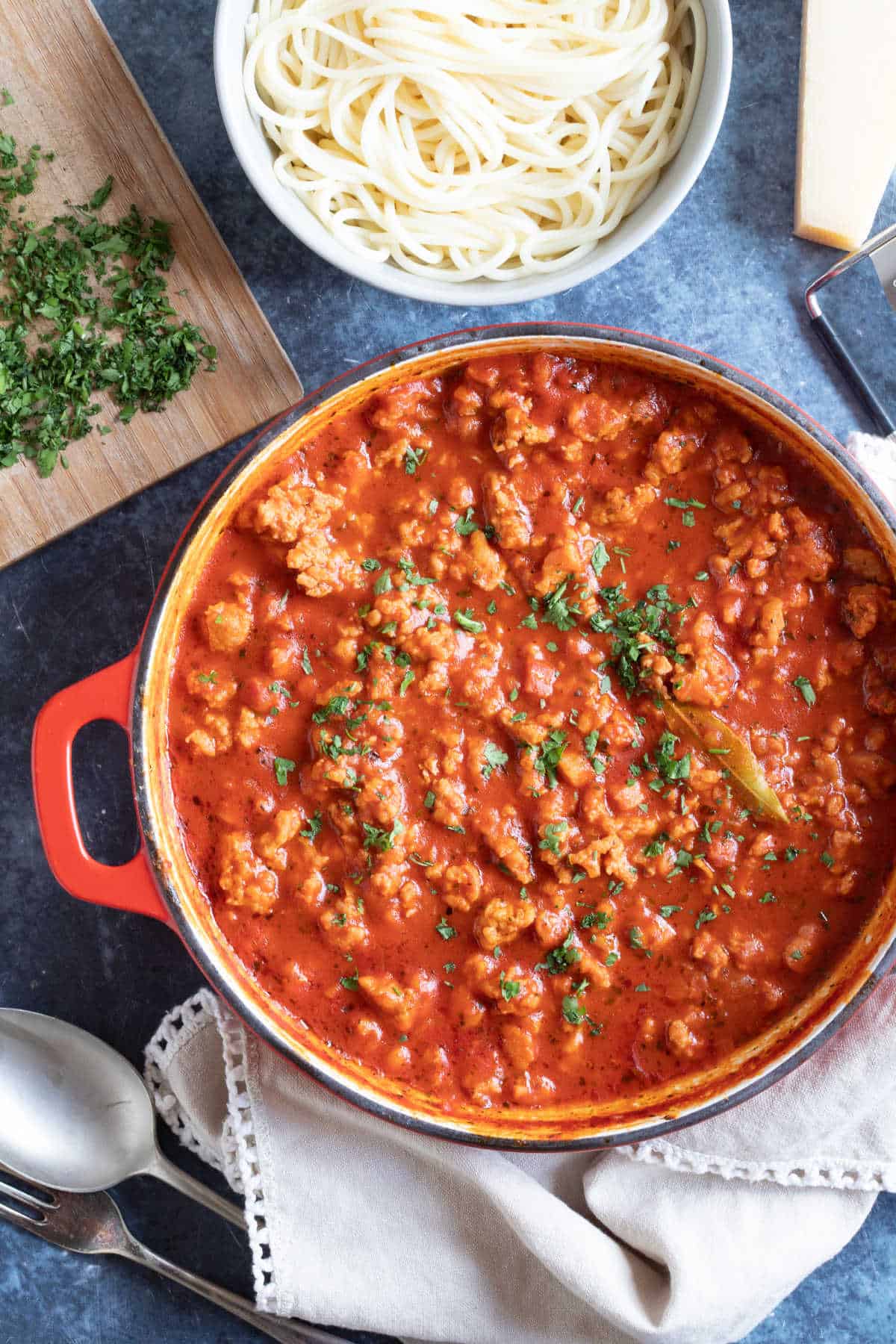 A pan of chicken bolognese with spaghetti and chopped herbs.