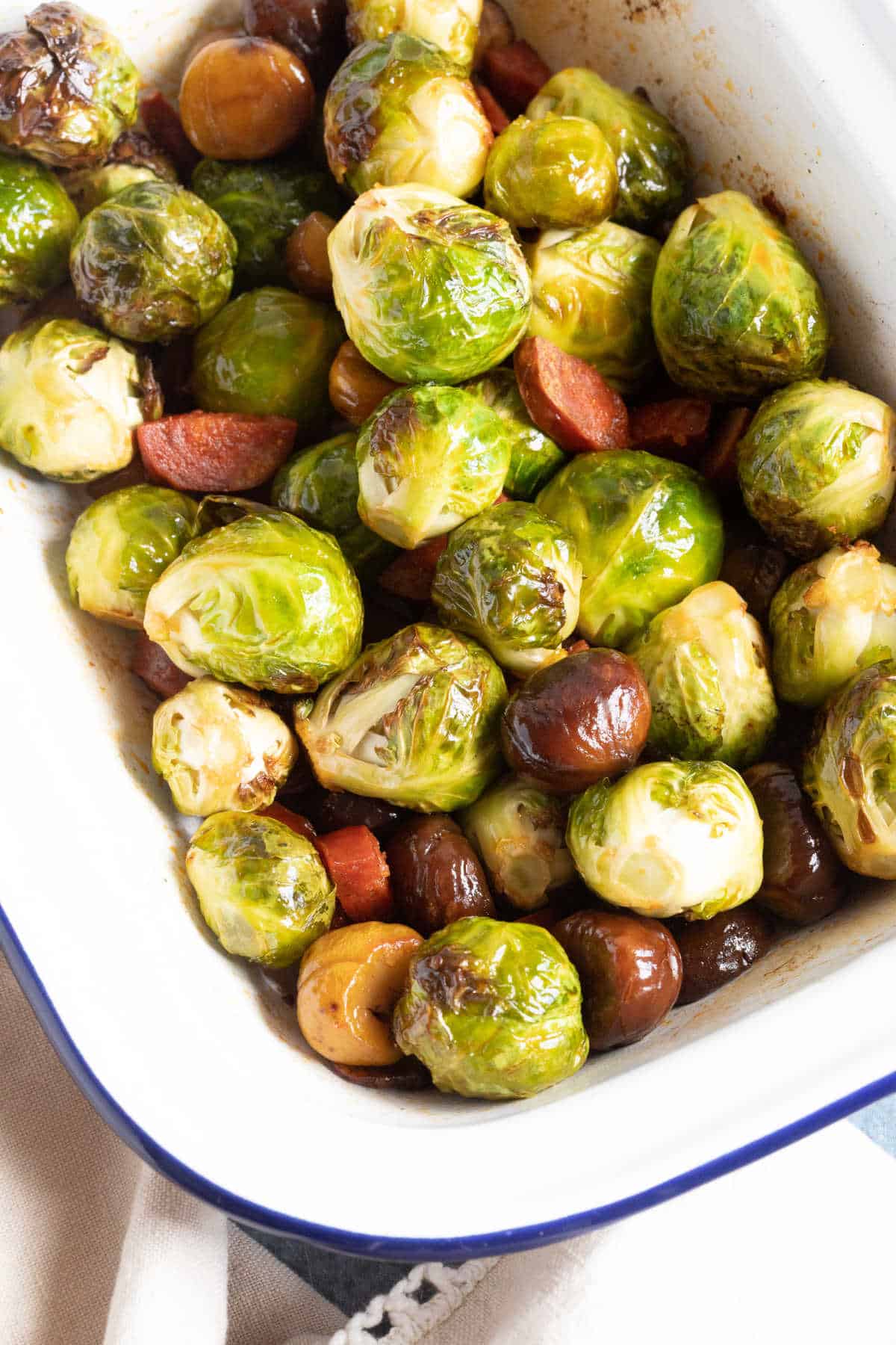 Roasted Brussels Sprouts in a white baking tin with chestnuts and chorizo.