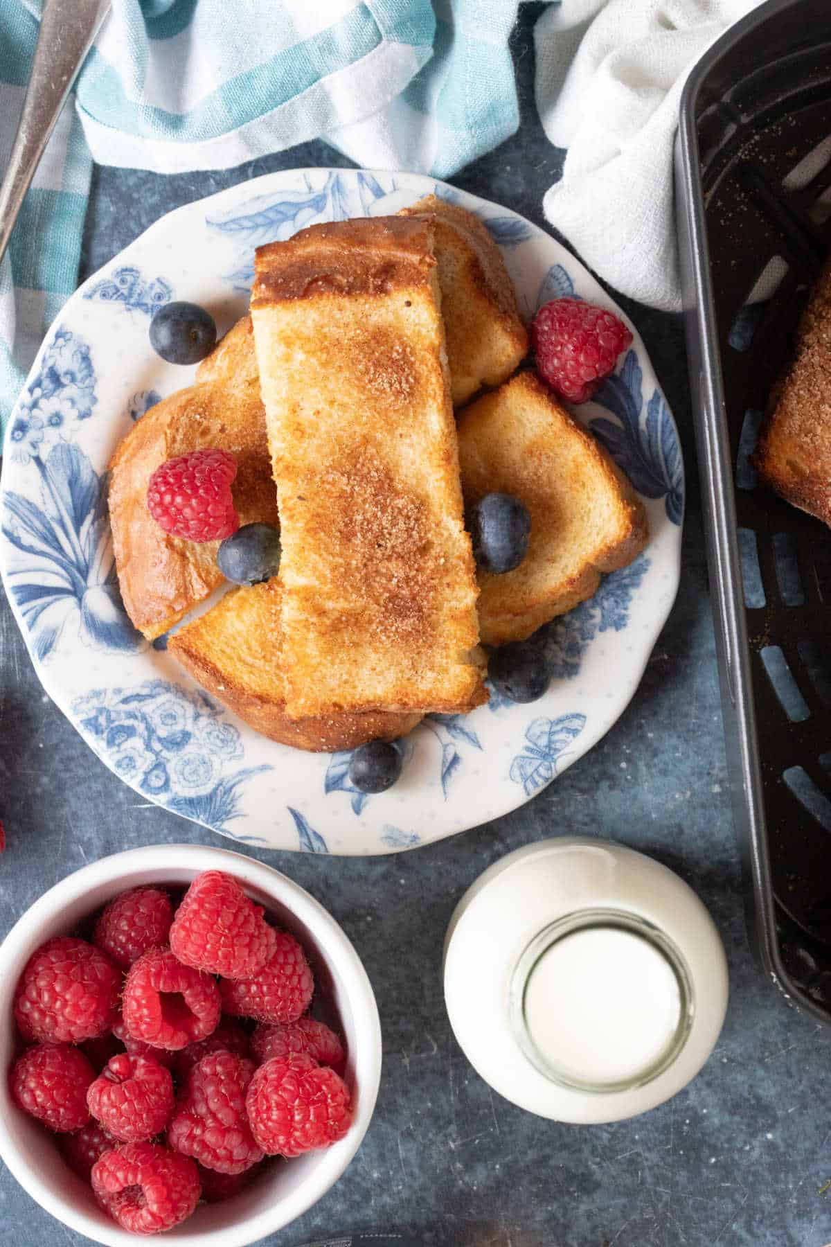Air fryer French toast sticks on a blue and white plate with fresh fruit.