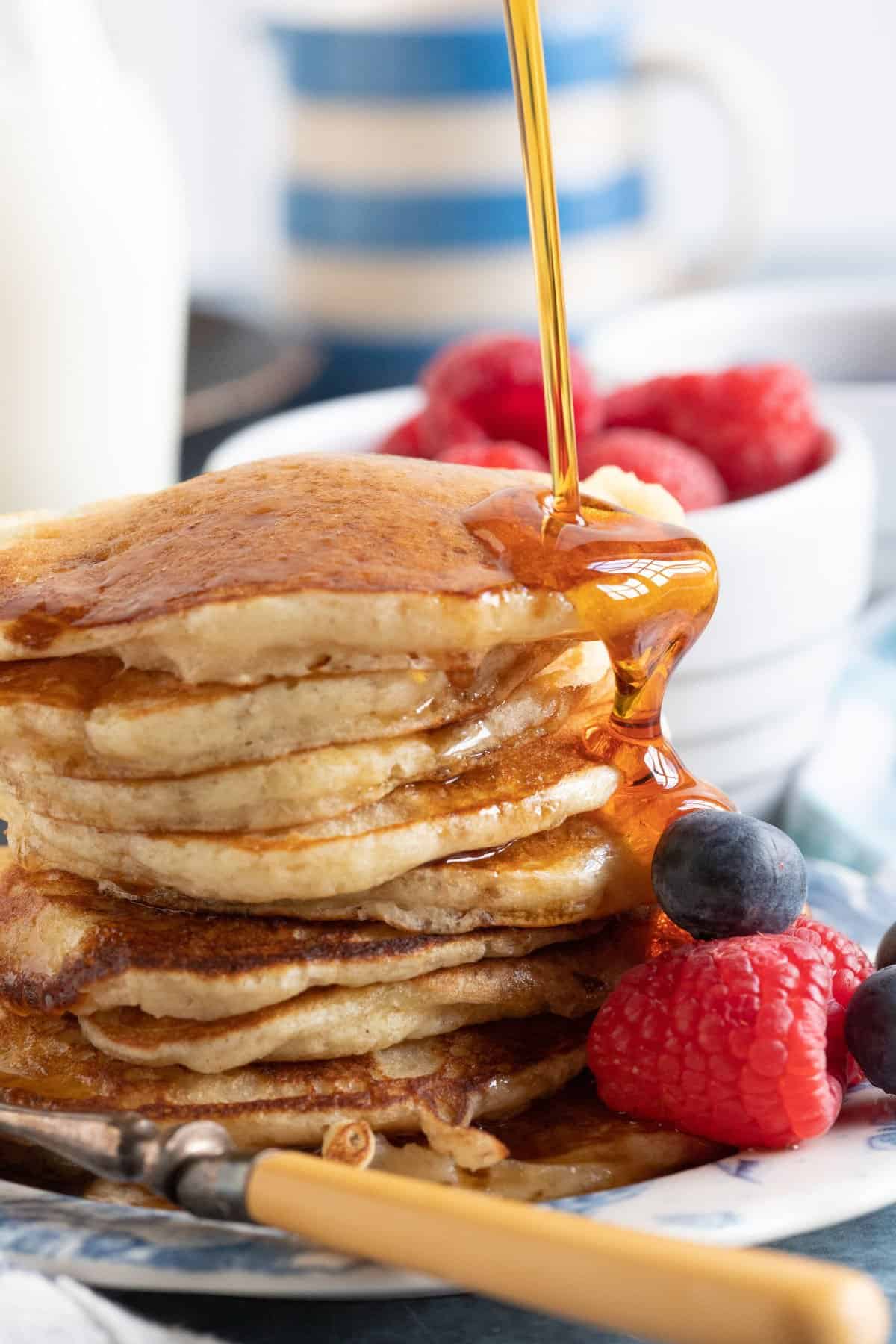 A stack of buttermilk pancakes with maple syrup poured on top.