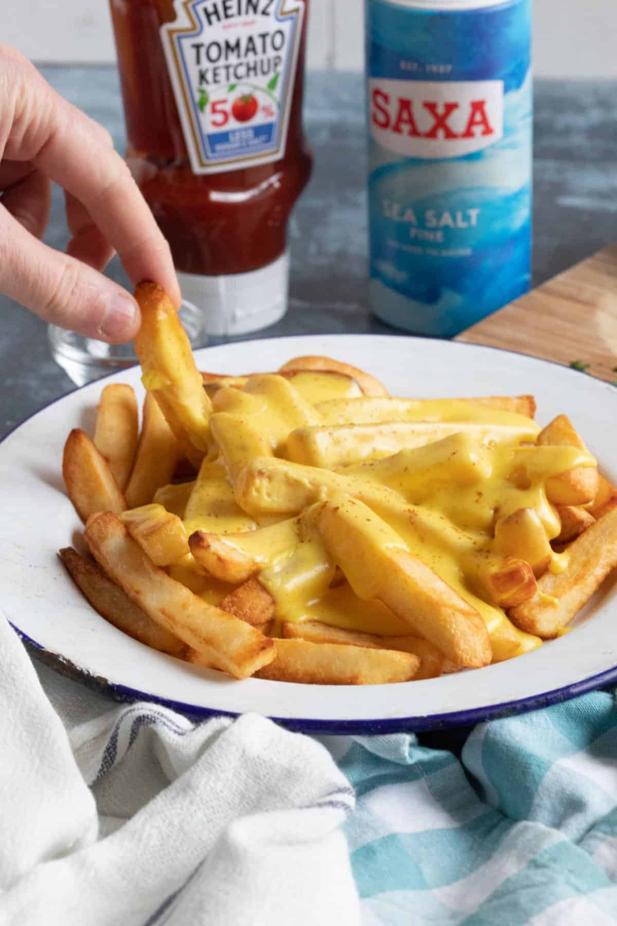 A plate of cheesy chips with salt and ketchup.