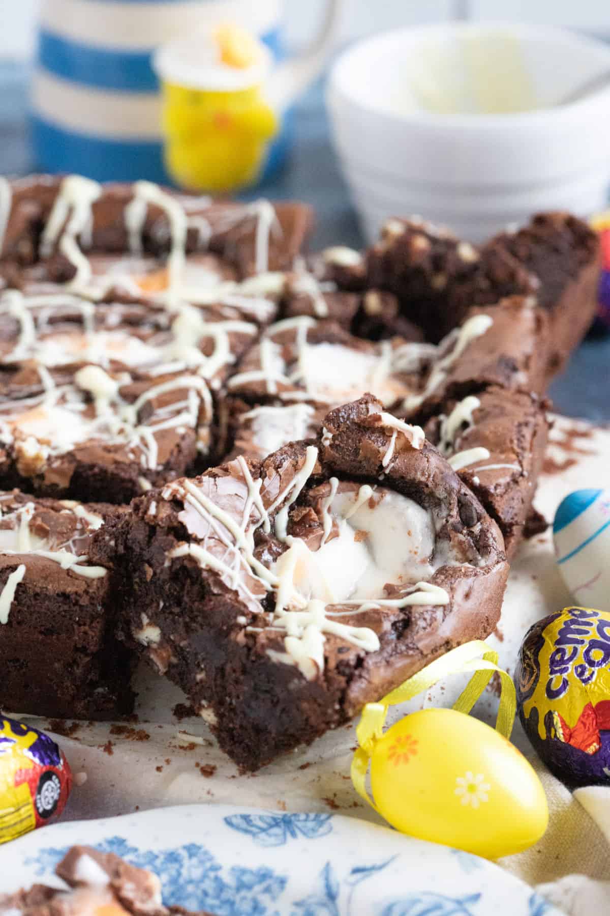 Creme egg brownies drizzled with white chocolate on a wooden board.