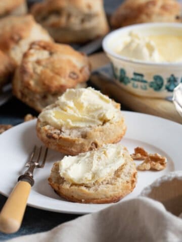 A date and walnut scone on a plate with clotted cream.