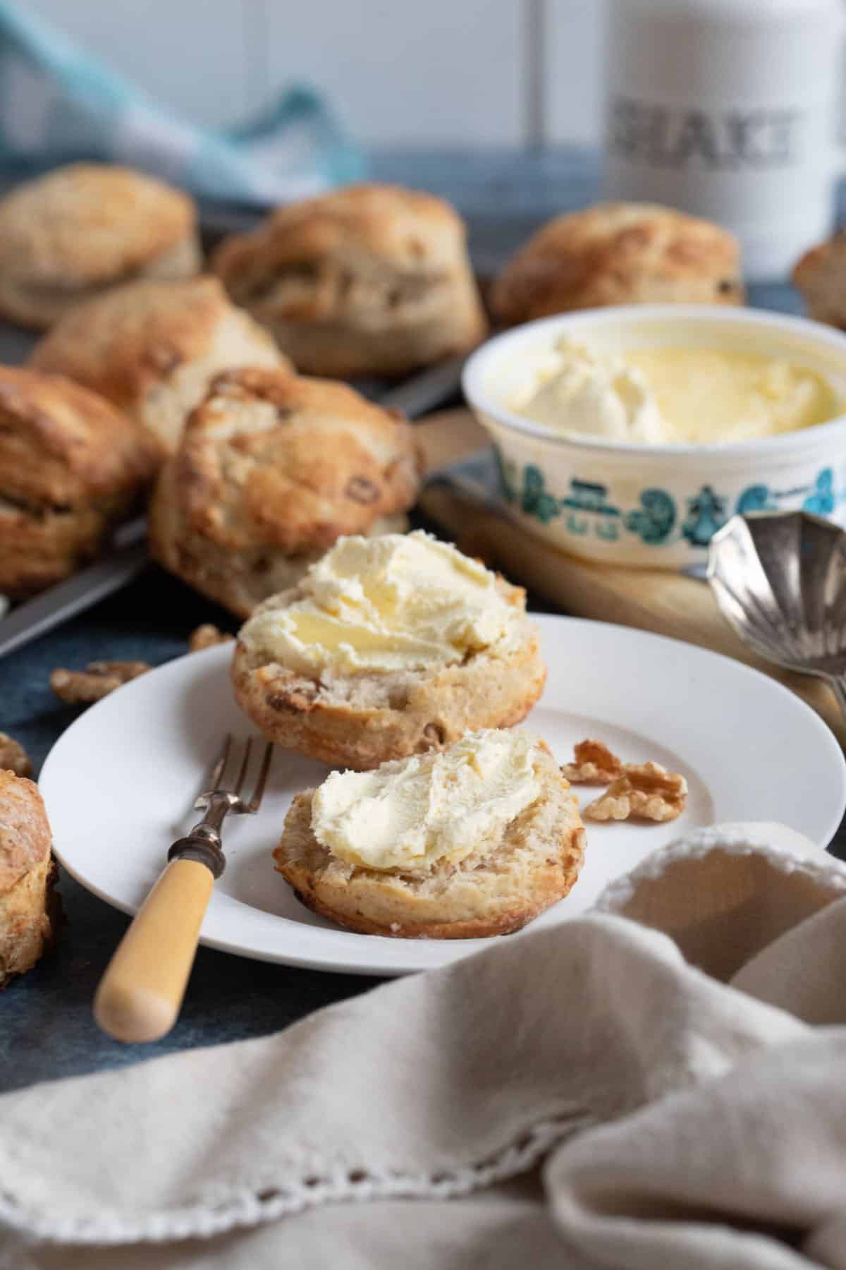 Freshly baked date and walnut scones. One scone is split open on a plate and served with clotted cream.