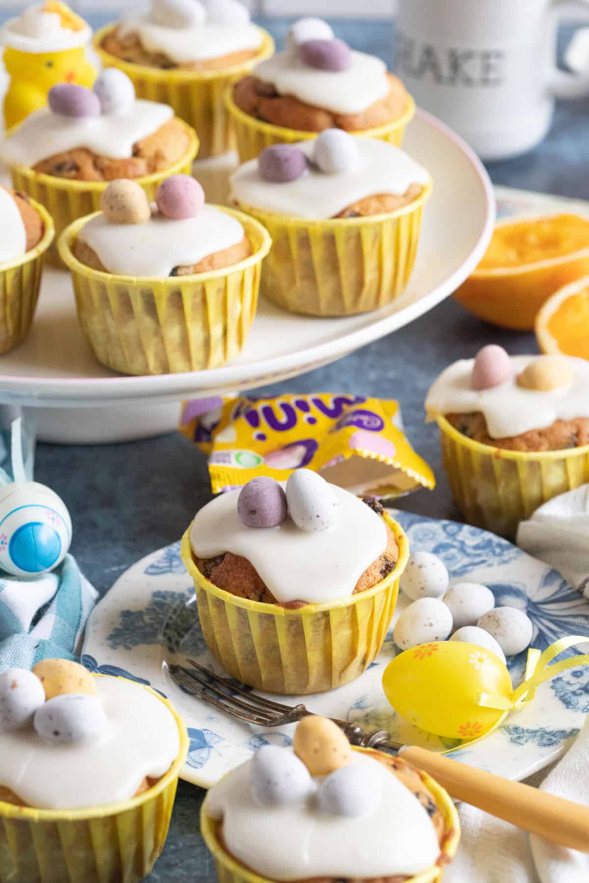 Easter simnel muffins on a cake stand and plate, topped with mini eggs.