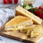 Cheese toastie made in an air fryer on a wooden board with crisps.