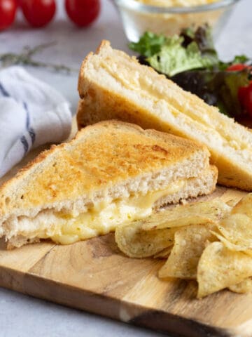 Cheese toastie made in an air fryer on a wooden board with crisps.