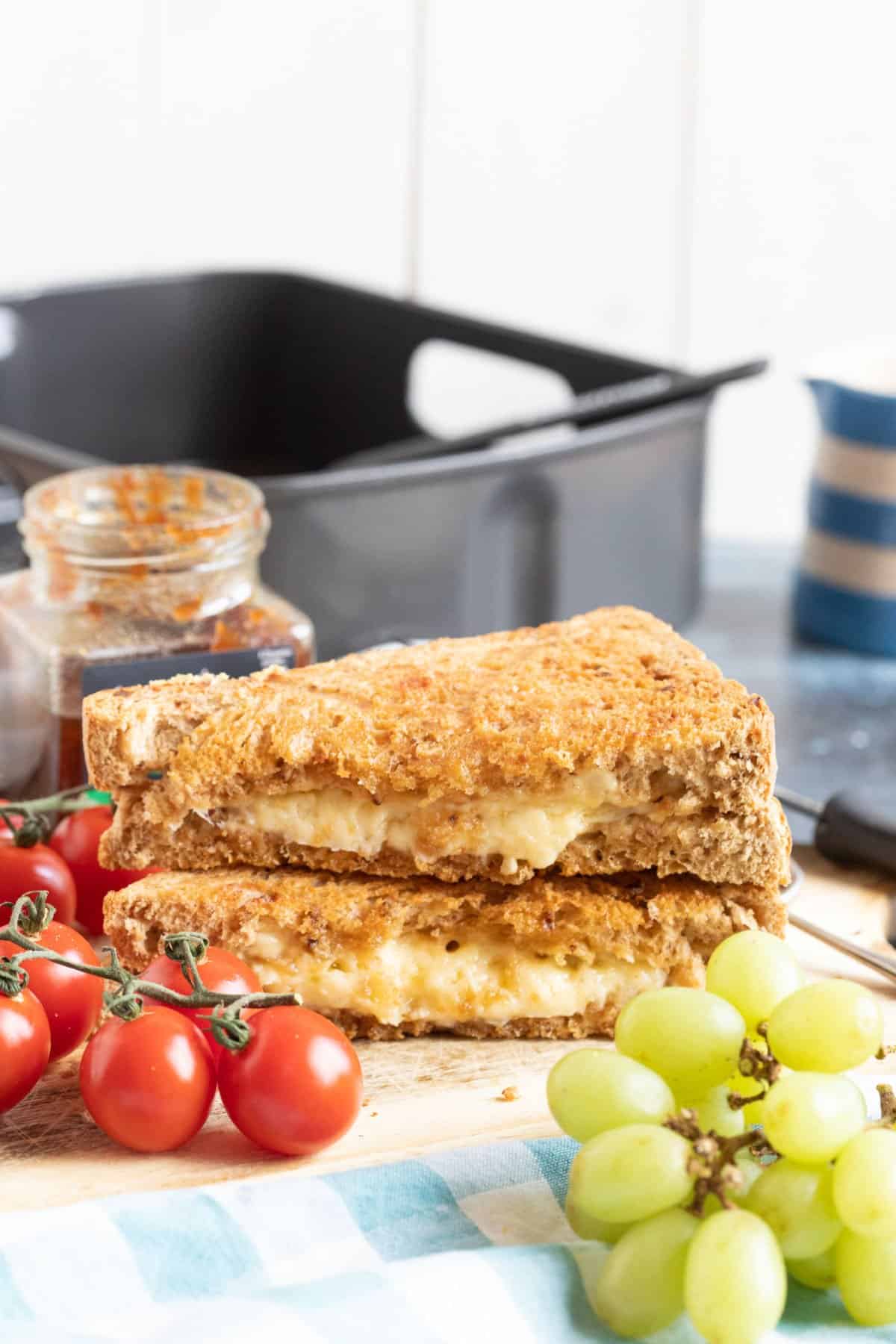 Cheese toastie on a wooden board with tomatoes and grapes.